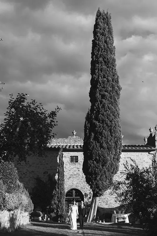 Newlyweds walk in the garden of the Relais il Falconiere in front of the large cypress tree