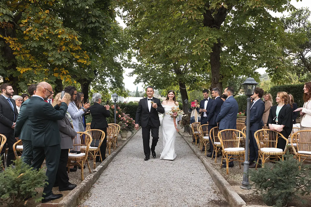 The bride and her father enter the garden of the Relais il Falconiere in Cortona for the wedding ceremony.